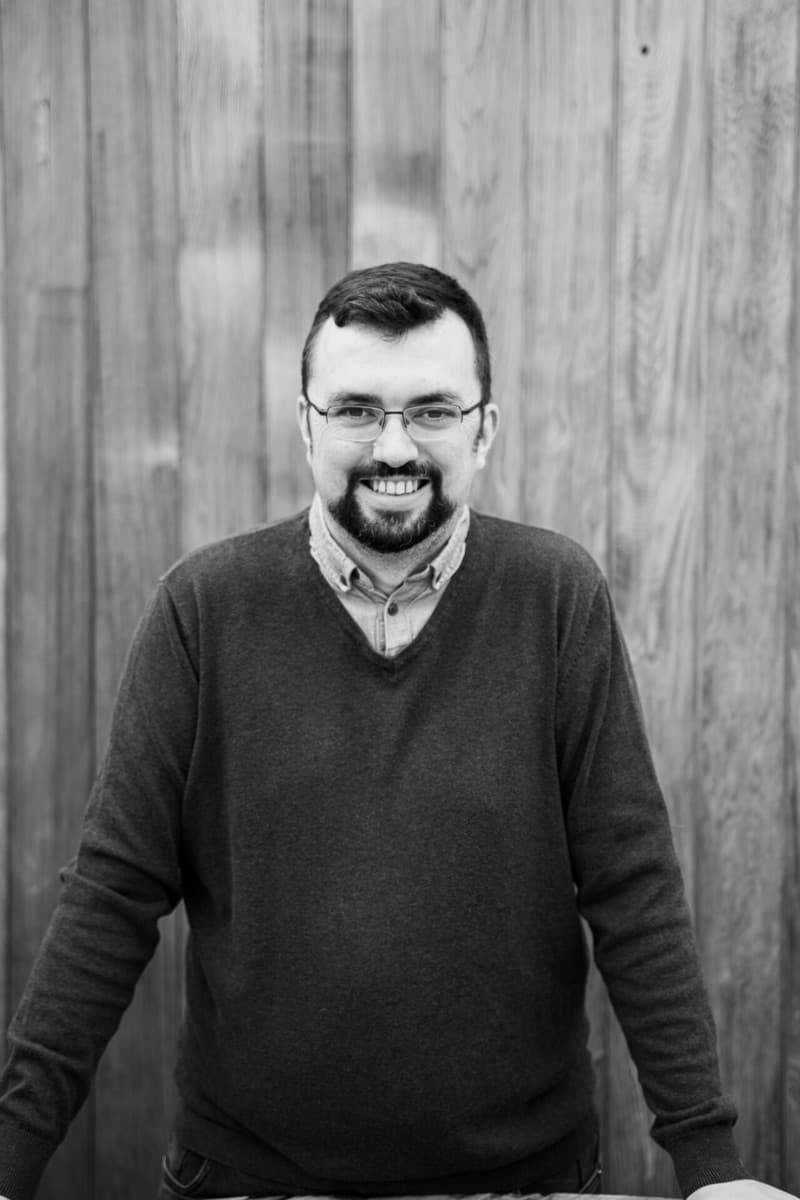 Portrait of Kristian Downer smiling in front of a wooden wall