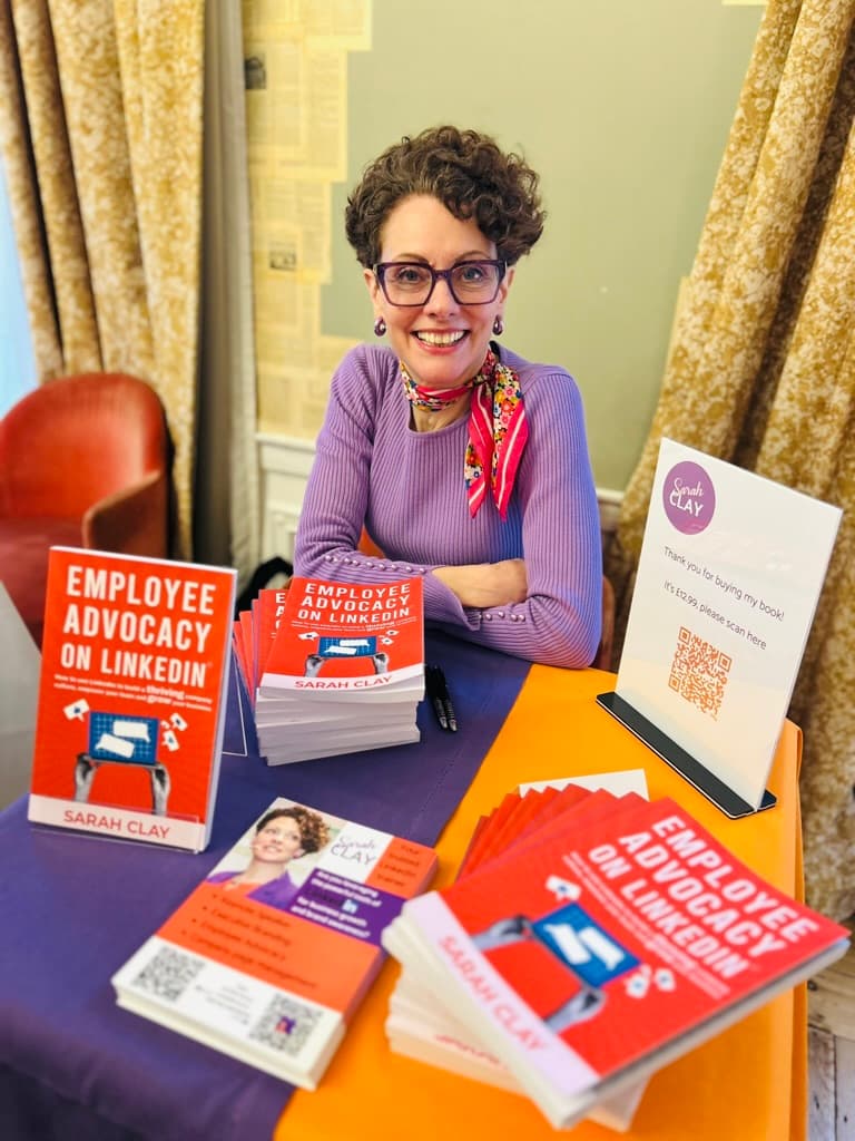 Sarah Clay at a signing table stacked with copies of her book Employee Advocacy on LinkedIn