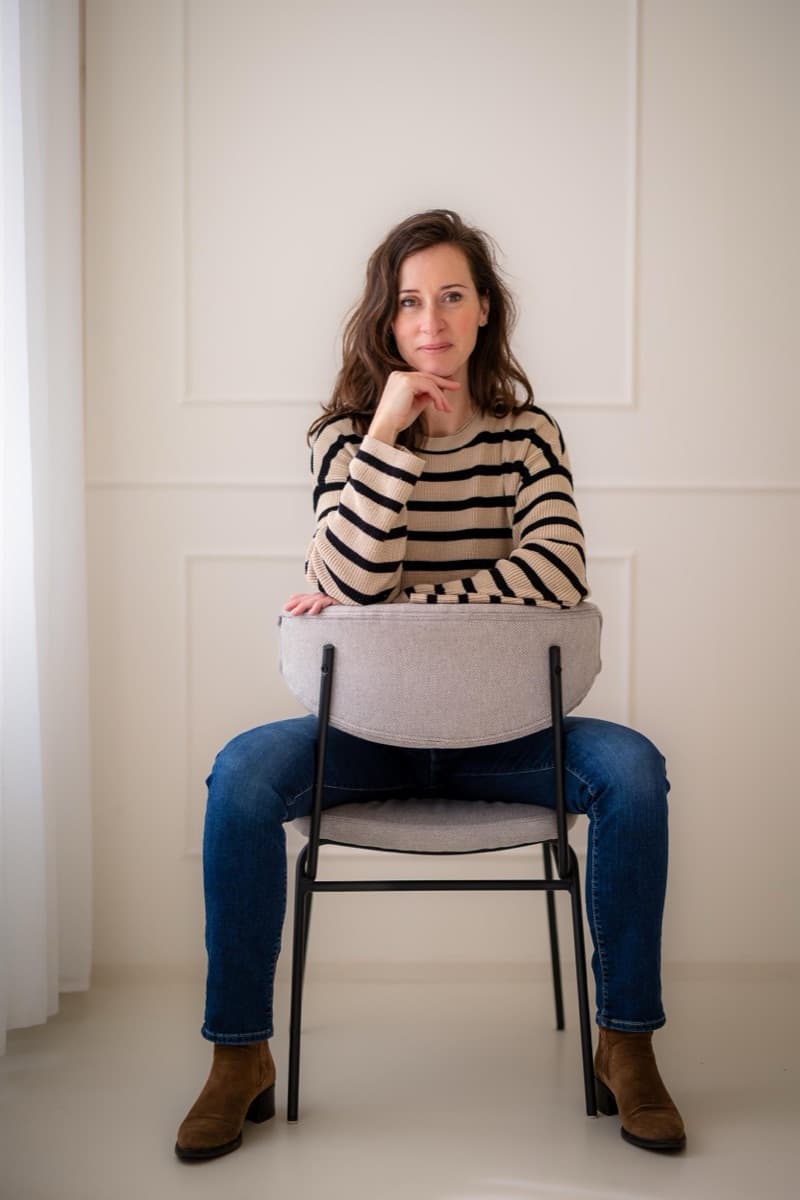 Ilse Weijland sitting backwards on a chair in a striped jumper